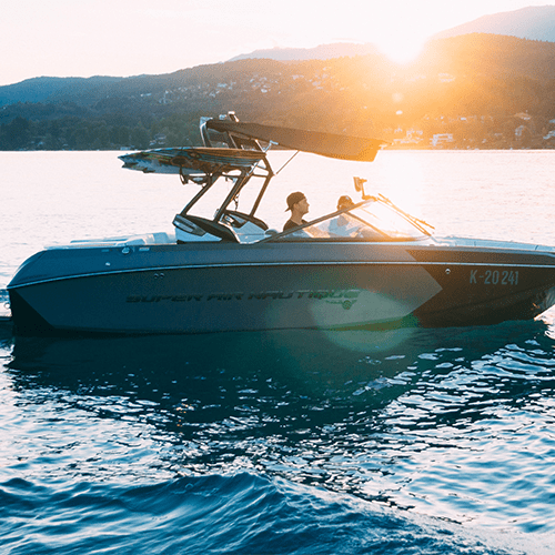 A boat floats in calm waters, with a sun setting behind a mountain in the distance.